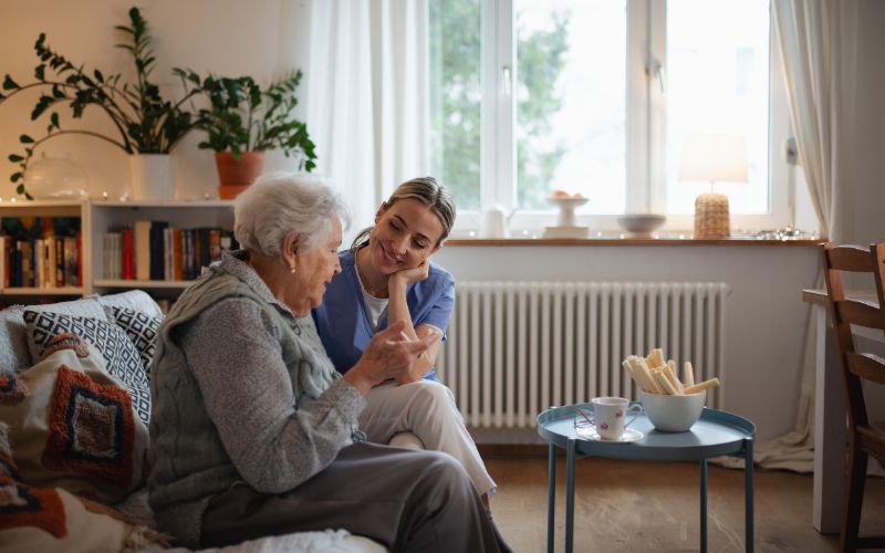 Jak umieścić Bliskiego w Domu Opieki – opiekunka trzyma za rękę uśmiechniętą Seniorkę
